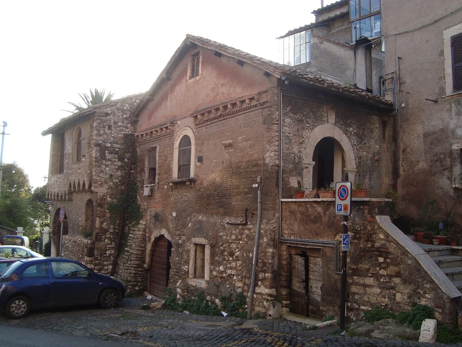 Case medievali in pietra e mattoni lungo una via acciottolata del centro storico di Tivoli, con un cartello di divieto di sosta e un'auto parcheggiata